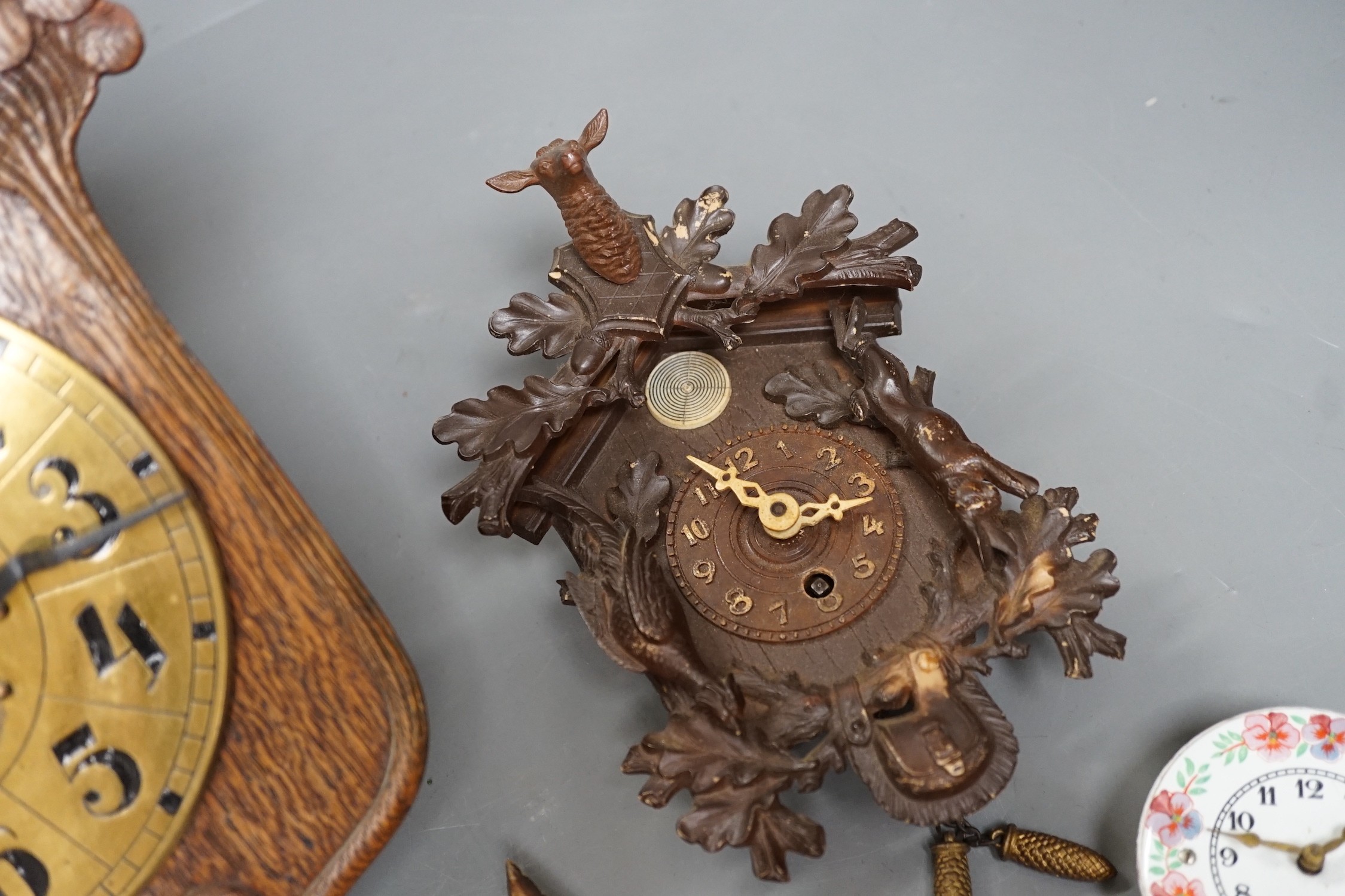 An early 20th century German Jugendstil oak wall timepiece, four miniature Black Forest timepieces and three floral enamelled examples, largest 23cms high